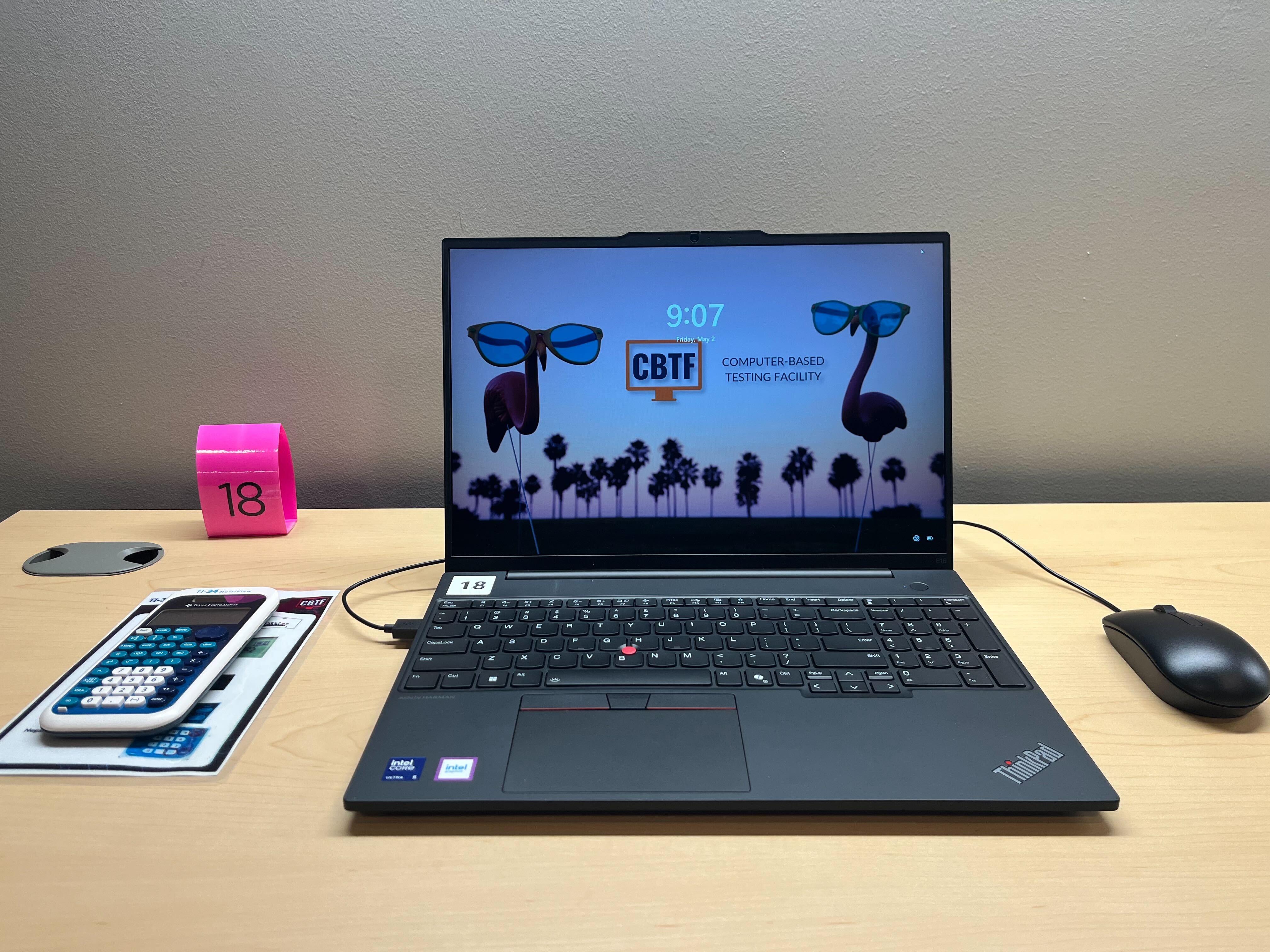 The picture shows a laptop centered on a desk with the CBTF flamingo background. To the left is a CBTF calculator and to the right is a computer mouse.